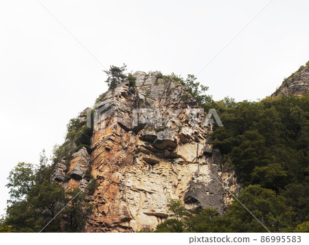 Steep cliffs covered with green vegetation against the backdrop of a white cloudy sky Steep cliffs covered with green vegetation against the backdrop of a white cloudy sky 86995583