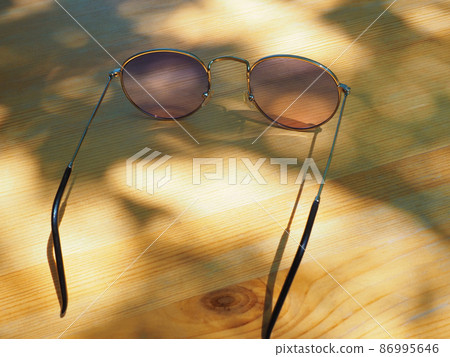 Sunglasses with pink transparent glasses lie on a wooden surface in the sunlight outdoors 86995646