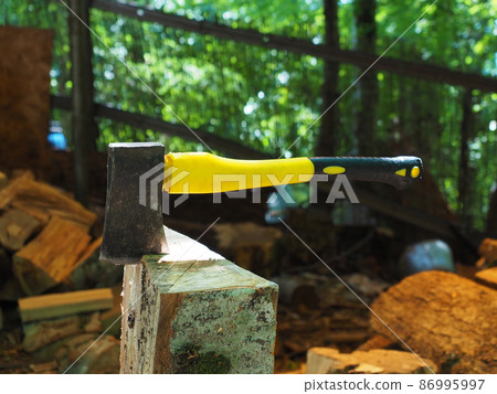 An ax with a yellow handle stuck into a log in a gazebo against a blurred background 86995997