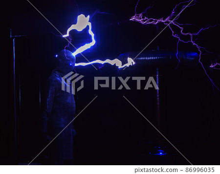 Huge electric coils spew lightning striking a man dressed in a chain suit. Electric show Huge electric coils spew lightning striking a man dressed in a chain suit. Electric show 86996035