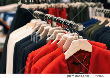 Woman jackets in red, blue, white and other colors on hangers in a retail clothes store. 86996800