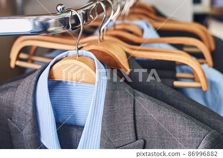 Mens suits and formal blue shirts on wooden hangers in a clothes store 86996882