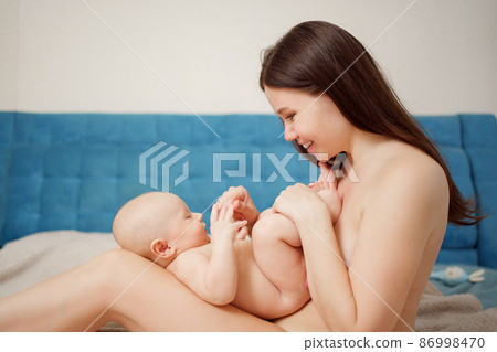 a naked mother plays with the baby on the bed. maternal and child health.  86998470