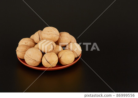 Many walnuts lie on a clay plate on a black background 86999556