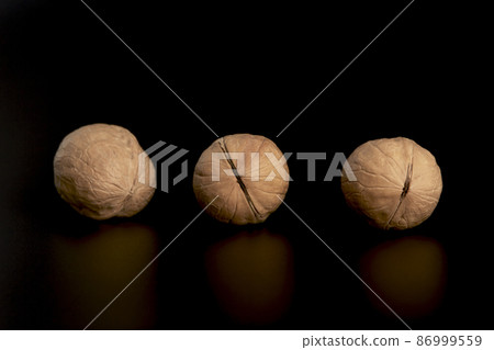 Three walnuts at a distance from each other on a black background Three walnuts at a distance from each other on a black background 86999559
