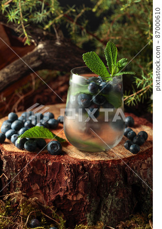 Cocktail with ice, blueberries, and mint on a pine stump in the forest. Cocktail with ice, blueberries, and mint on a pine stump in the forest. 87000610