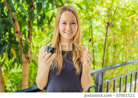 Young woman brush teeth using Activated charcoal powder for brushing and whitening teeth. Bamboo eco brush 87001521