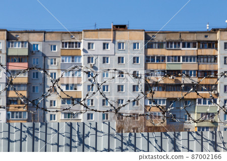 residential multi-storey building behind a fence with barbed wire at daylight, the concept of imprisonment, restriction of freedom, quarantine 87002166
