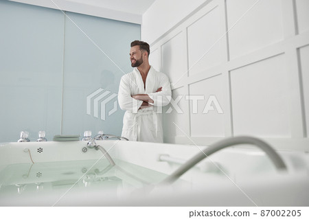 Attractive man with crossed arms stands near hydro massage tub in spa salon Attractive man with crossed arms stands near hydro massage tub in spa salon 87002205