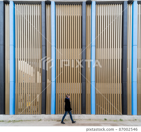 Pedestrian woman walking in front of a colorful Industrial background with straight patterned vertical lines, Brussels Pedestrian woman walking in front of a colorful Industrial background with straight patterned vertical lines, Brussels 87002546