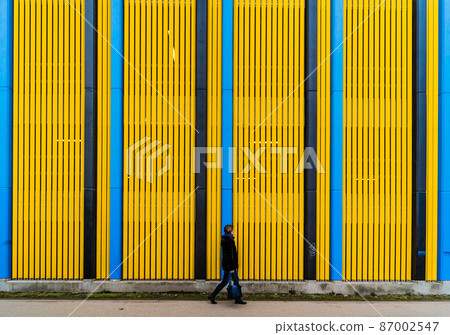 Pedestrian woman walking in front of a colorful Industrial background with straight patterned vertical lines, Brussels 87002547