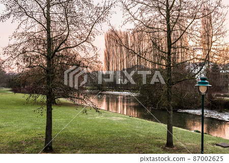 Idyllic view over a pond, bare trees and meadows covered with a thin snowlayer in the Baudouin park during sunrise, Jette, Belgium Idyllic view over a pond, bare trees and meadows covered with a thin snowlayer in the Baudouin park during sunrise, Jette, Belgium 87002625