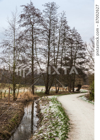 Idyllic view over the Baudouin park with a walking path along the Molenbeek creek and bare trees in winter, Belgium 87002627