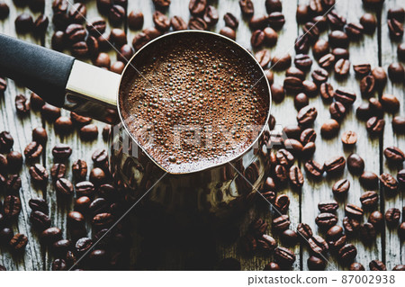 Turkish coffee in coffee pot, coffee beans scattered on wooden table, high angle view Turkish coffee in coffee pot, coffee beans scattered on wooden table, high angle view 87002938