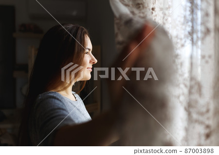 Pretty young woman in apartment opening window curtains after wake up, enjoying morning sunshine .Mental health concept . Pretty young woman in apartment opening window curtains after wake up, enjoying morning sunshine .Mental health concept . 87003898