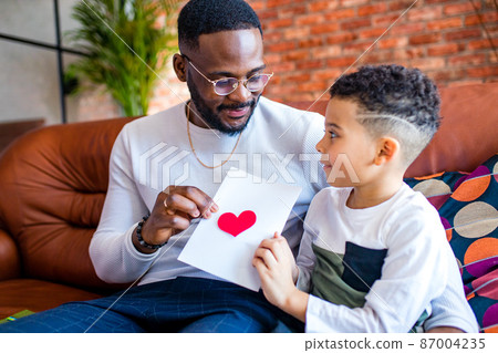 afro american baby giving to dad a Valentine's Day picture in living room afro american baby giving to dad a Valentine's Day picture in living room 87004235