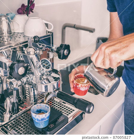Making making coffee at home with espresso machine pouring steamed milk in cup. Kitchen breakfast lifestyle. Square crop 87005827