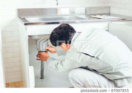 A man in work clothes checking the drain under the sink A man in work clothes checking the drain under the sink 87007855