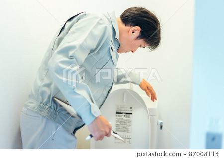 A man in work clothes checking the toilet 87008113