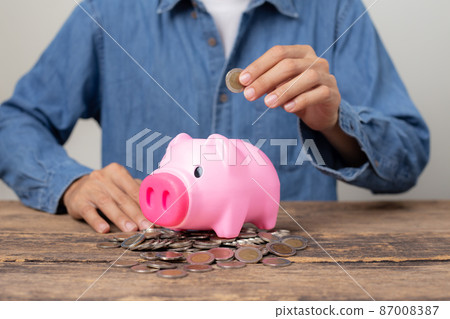 Closeup Man hand putting coin into a piggy bank, Concept of saving money and business investment. 87008387