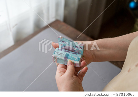 A grown woman counts money indoors. Her hands are holding a bundle of Ukrainian hryvnias. Banknotes in denominations of 1000 hryvnia. Selective focus A grown woman counts money indoors. Her hands are holding a bundle of Ukrainian hryvnias. Banknotes in denominations of 1000 hryvnia. Selective focus 87010063