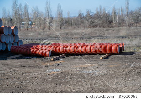Stack of new orange polypropylene pipes in front of the railroad. Plastic pipes for laying in the gutter. Industrial warehouse. 87010065
