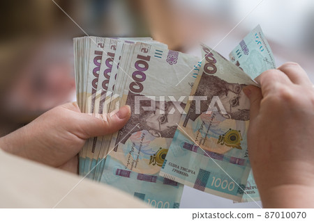 A woman's hands are holding a bundle of Ukrainian hryvnias. Banknotes in denominations of 1000 hryvnia. Close-up. Selective focus. A woman's hands are holding a bundle of Ukrainian hryvnias. Banknotes in denominations of 1000 hryvnia. Close-up. Selective focus. 87010070