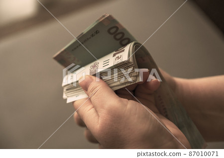 A grown woman counts money indoors. Her hands are holding a bundle of Ukrainian hryvnias. Banknotes in denominations of 1000 hryvnia. Selective focus A grown woman counts money indoors. Her hands are holding a bundle of Ukrainian hryvnias. Banknotes in denominations of 1000 hryvnia. Selective focus 87010071
