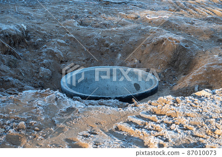Concrete ring for a water well in the frozen ground. There is an iron-concrete product in the excavated hole. The top layer of soil is covered with frost. Concrete ring for a water well in the frozen ground. There is an iron-concrete product in the excavated hole. The top layer of soil is covered with frost. 87010073