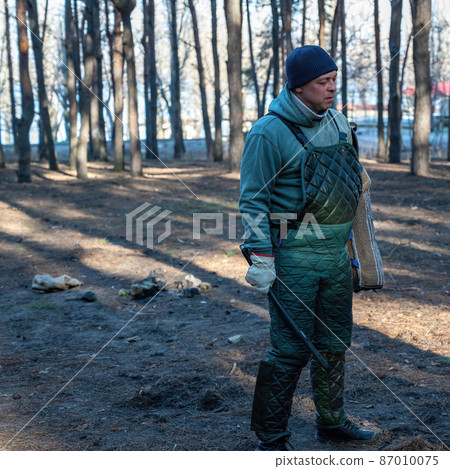 Full-length portrait of a canine instructor for training dogs for protective guard duty. A mature man standing in special overalls, holding a baton and bite sleeve. Full-length portrait of a canine instructor for training dogs for protective guard duty. A mature man standing in special overalls, holding a baton and bite sleeve. 87010075