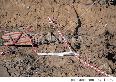 Fallen wooden fence and barrier tape. Fence with prohibition and warning signs lies on the ground. Buried ditch. Daytime. Fallen wooden fence and barrier tape. Fence with prohibition and warning signs lies on the ground. Buried ditch. Daytime. 87010079