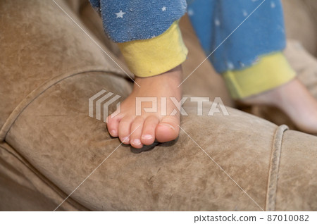 Close-up of a child's bare feet. The 5-year-old grandson has just woken up and is standing on the armrest of the couch. Close-up of a child's bare feet. The 5-year-old grandson has just woken up and is standing on the armrest of the couch. 87010082