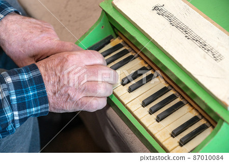 An elderly man plays a toy piano. Hands press the keys of an old children's instrument. An elderly man plays a toy piano. Hands press the keys of an old children's instrument. 87010084