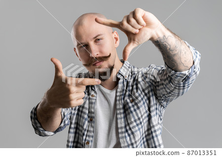 Closeup of creative bald bearded photographer who making frame with fingers in front of face Closeup of creative bald bearded photographer who making frame with fingers in front of face 87013351