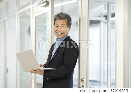 A smiling man in his 60s holding a laptop, a senior businessman 87014295