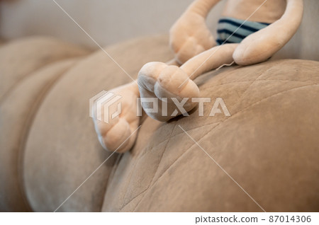 The bottom section of a child's stuffed toy. A beige toy sitting on the couch. 87014306