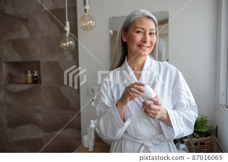 Pretty Asian woman holding cosmetic jar in the bathroom Pretty Asian woman holding cosmetic jar in the bathroom 87016065