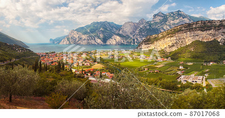 Lake coast with mountains and cliffs around, in the foreground village, green meadows and fields. Lago di garda near the Alps - Trombole, Riva del garda. 87017068