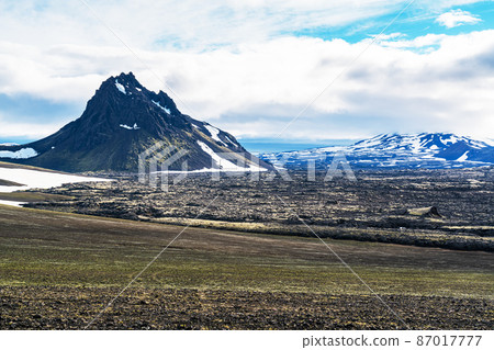 Beautiful volcanic landscape with snow covered mountain and rough lava rocks ground. 87017777
