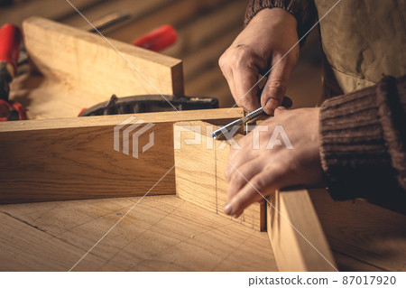 A man makes wood products with the help of special tools. Portrait of a young carpenter at work. Employment in the woodworking industry A man makes wood products with the help of special tools. Portrait of a young carpenter at work. Employment in the woodworking industry 87017920