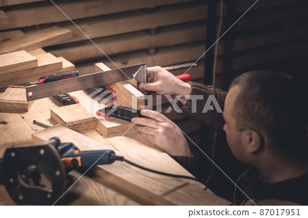 A man makes wood products with the help of special tools. Portrait of a young carpenter at work. Employment in the woodworking industry 87017951