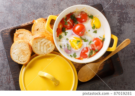 Eggs en Cocotte baked with tomato, parsley, meat, cheese closeup in the wooden tray. Horizontal top view 87019281