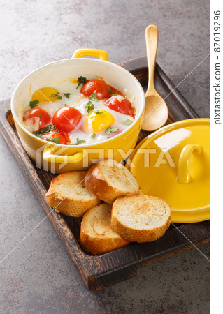 Oeufs cocotte is a French way of baking eggs in a water bath in the oven closeup in the wooden tray. Vertical 87019296