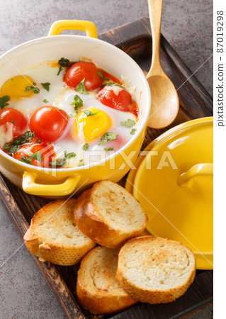 Egg cocotte with cheese and vegetables served with fresh parsley and toast closeup in the wooden tray. Vertical Egg cocotte with cheese and vegetables served with fresh parsley and toast closeup in the wooden tray. Vertical 87019298