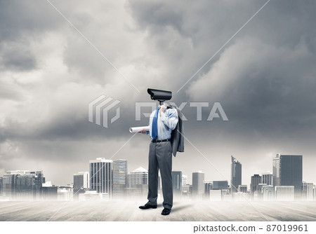 Camera headed man standing on wooden floor against modern cityscape Camera headed man standing on wooden floor against modern cityscape 87019961