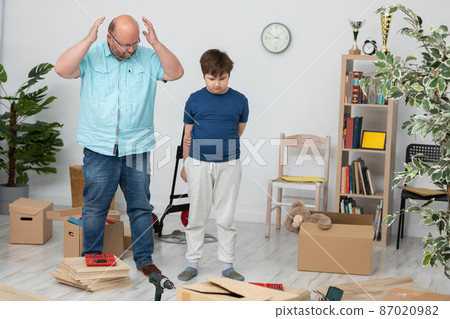 The father puts his hands up and the son looks at the mess in the room. 87020982