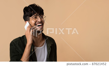 Happy middle eastern guy having phone conversation on beige 87021452
