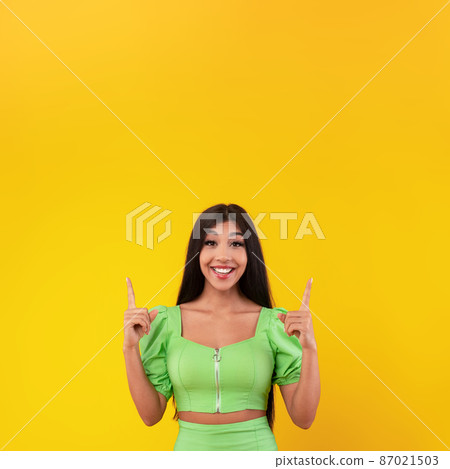 Excited woman pointing finger up at copy space 87021503