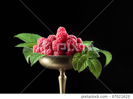 Fresh raspberries with leaves in an old brass dish. 87021628