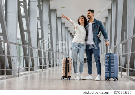 Travel Advertisement. Happy Middle Eastern Couple Standing In Airport And Pointing Aside Travel Advertisement. Happy Middle Eastern Couple Standing In Airport And Pointing Aside 87021633